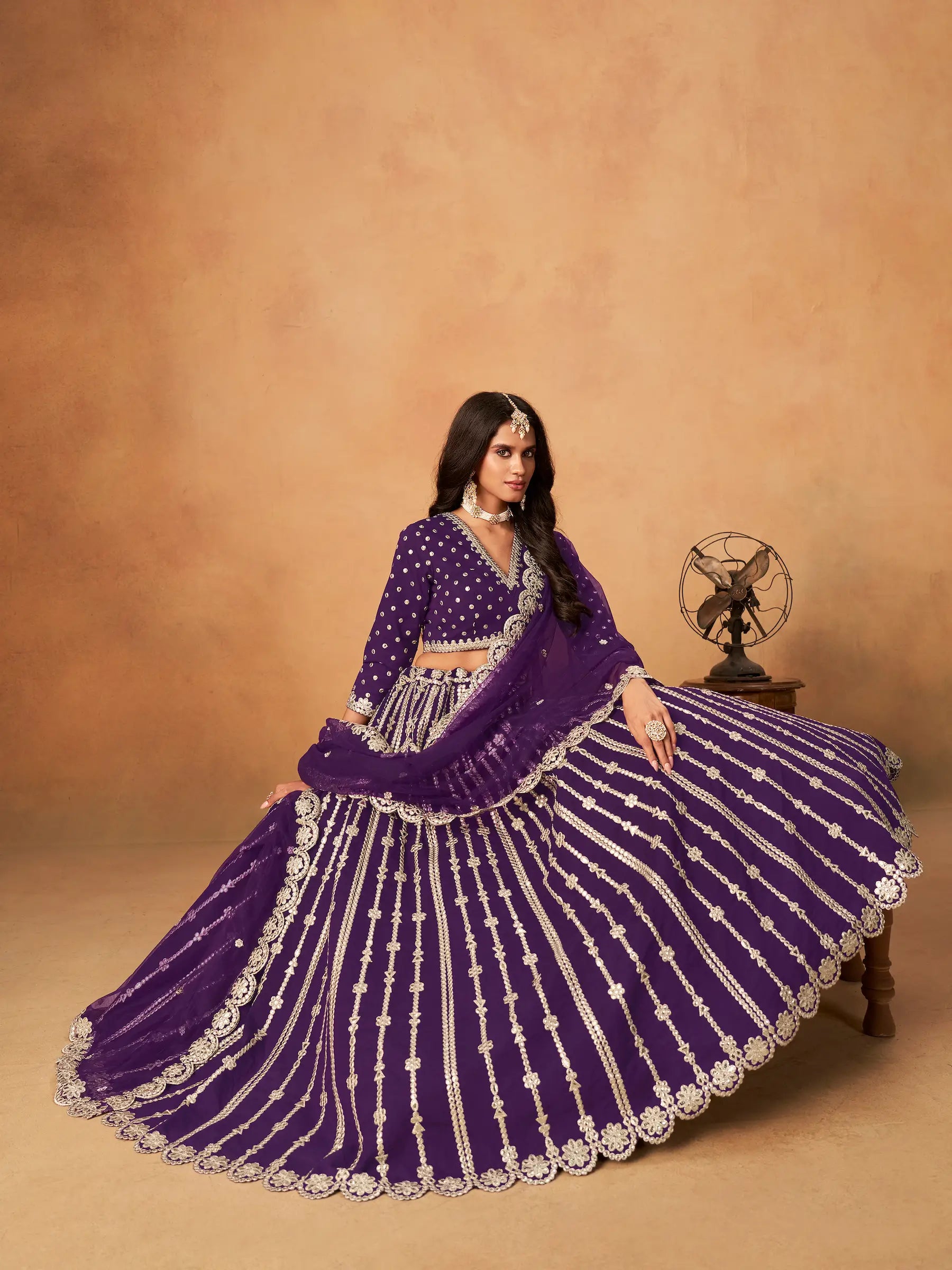 Model sitting wearing purple art silk lehenga choli with paper mirror and embroidery work