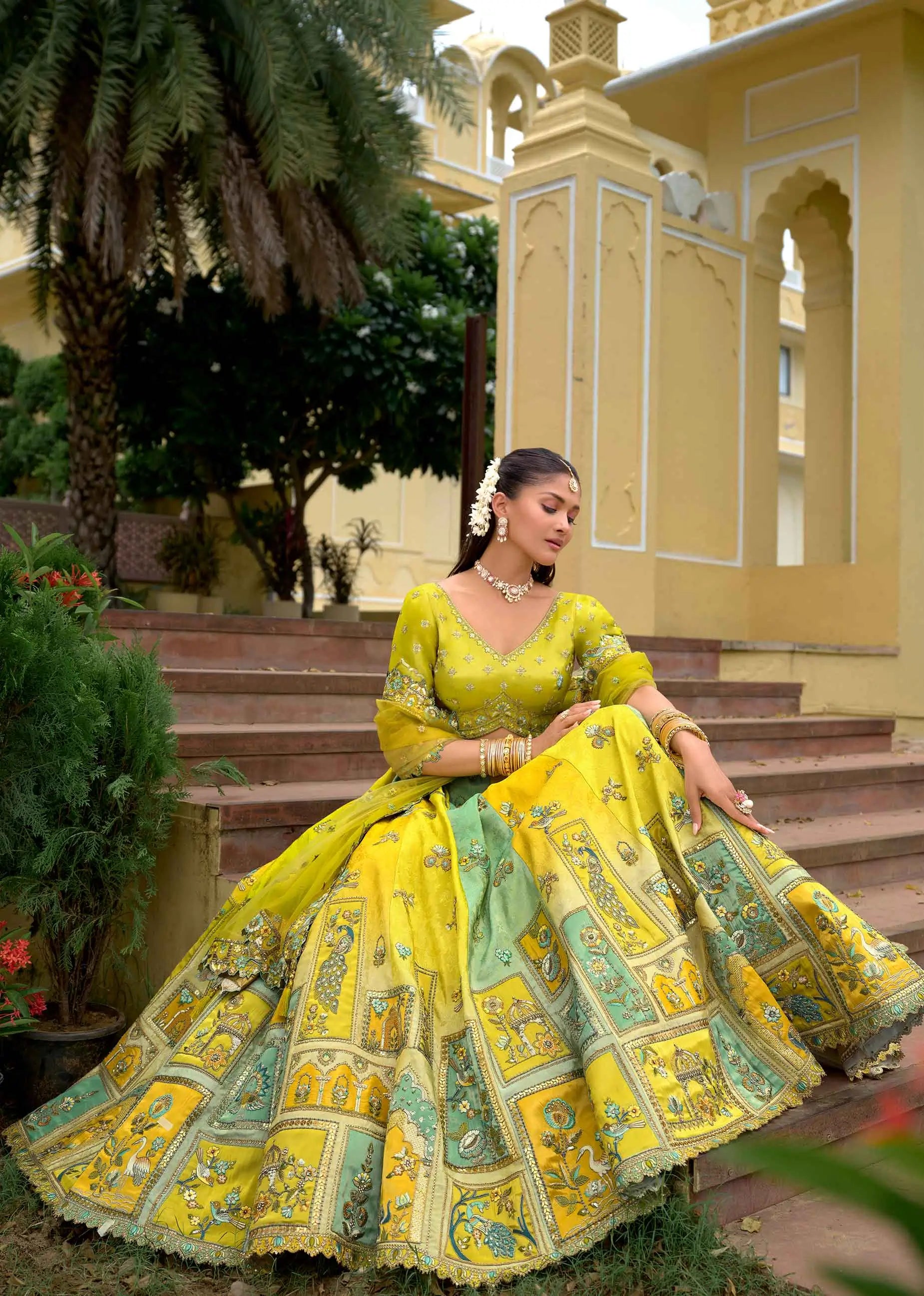 Model sitting wearing pastel olive designer lehenga with detailed embroidery work