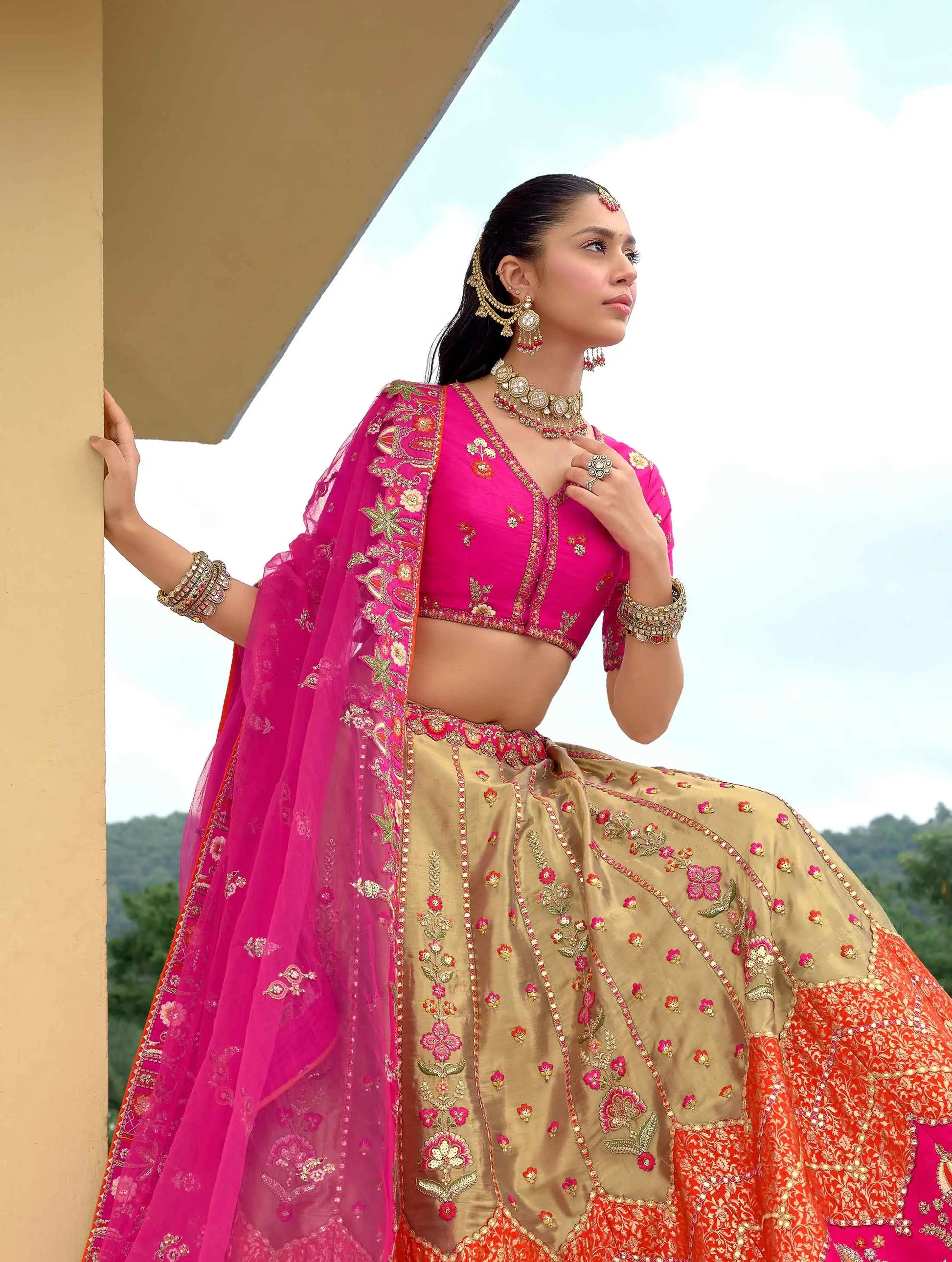 Model sitting wearing designer dark pink lehenga with detailed embroidery work